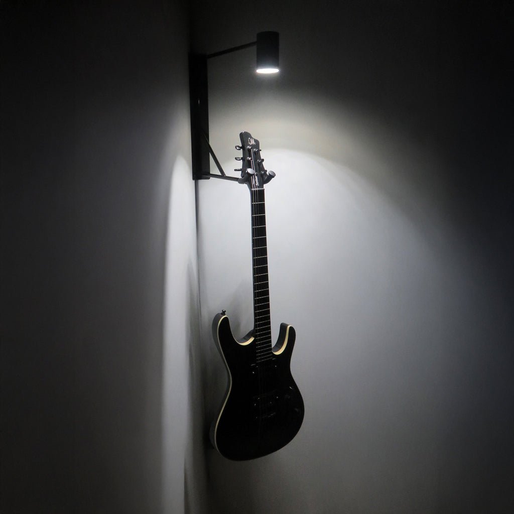 Schwarze Gitarre an Eck-Wandhalter mit weißer LED-Beleuchtung in der Dunkelheit