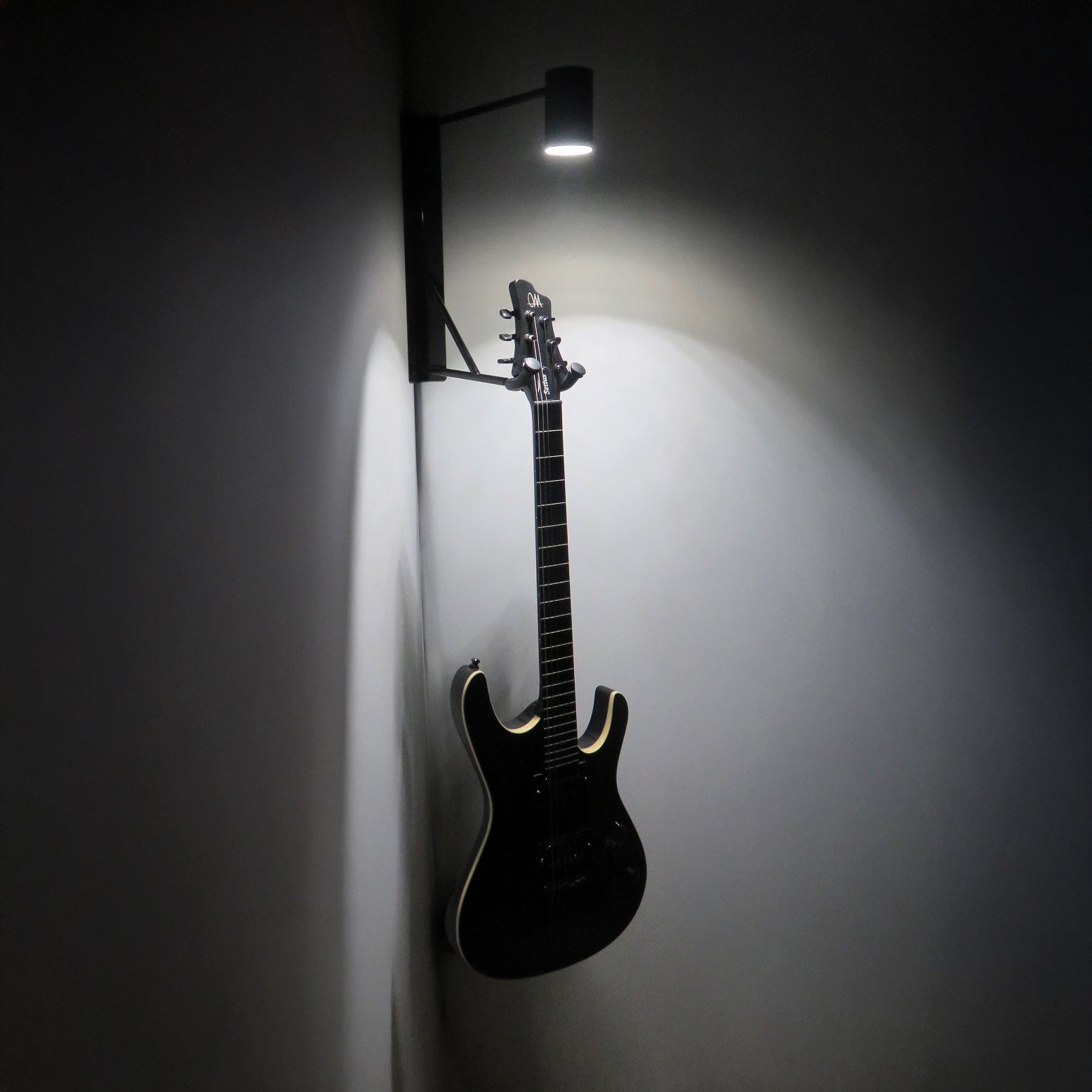 Schwarze Gitarre an Eck-Wandhalter mit weißer LED-Beleuchtung in der Dunkelheit